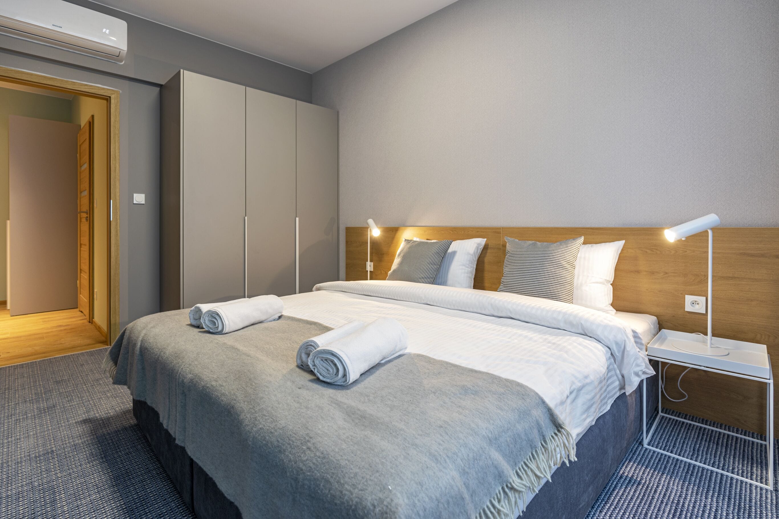 A hotel room with a bed, a wardrobe, a bedside table with a lamp, and a door.