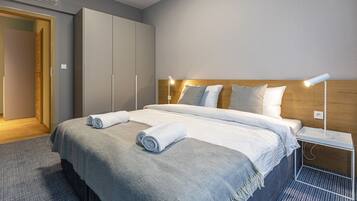 A hotel room with a bed, a wardrobe, a bedside table with a lamp, and a door.
