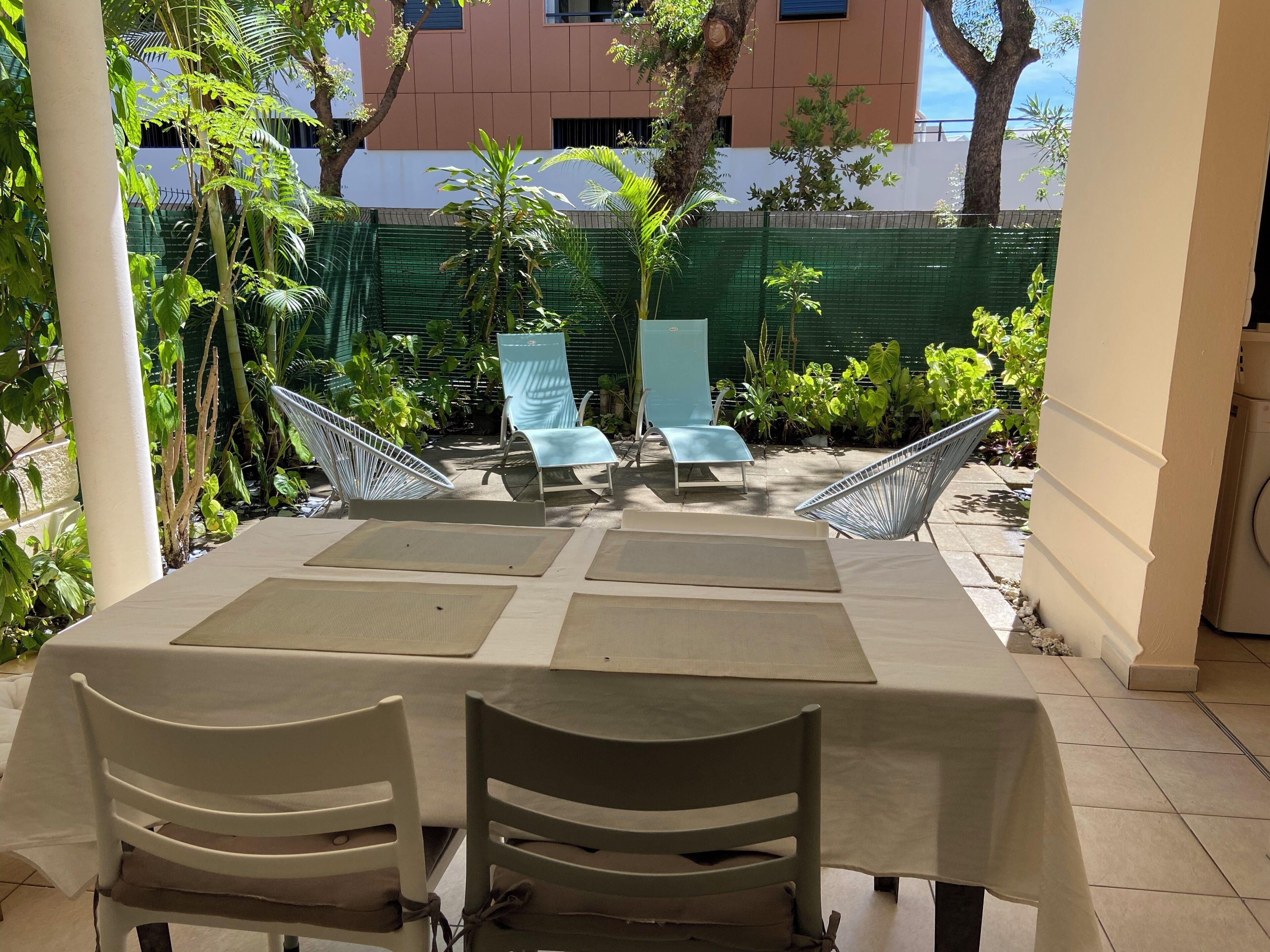Een terras buiten met een tafel gedekt voor twee personen, omringd door stoelen en een hangmat.