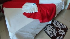 A neatly made bed with white and red bedding, a decorative pillow, and a patterned rug on a tiled floor.