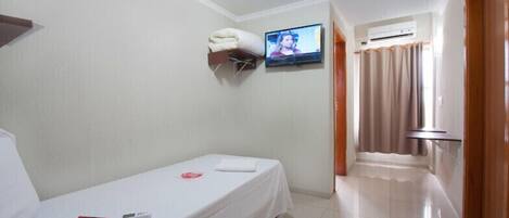 A small, clean room with a single bed, a TV mounted on the wall, and a bathroom visible through a door.