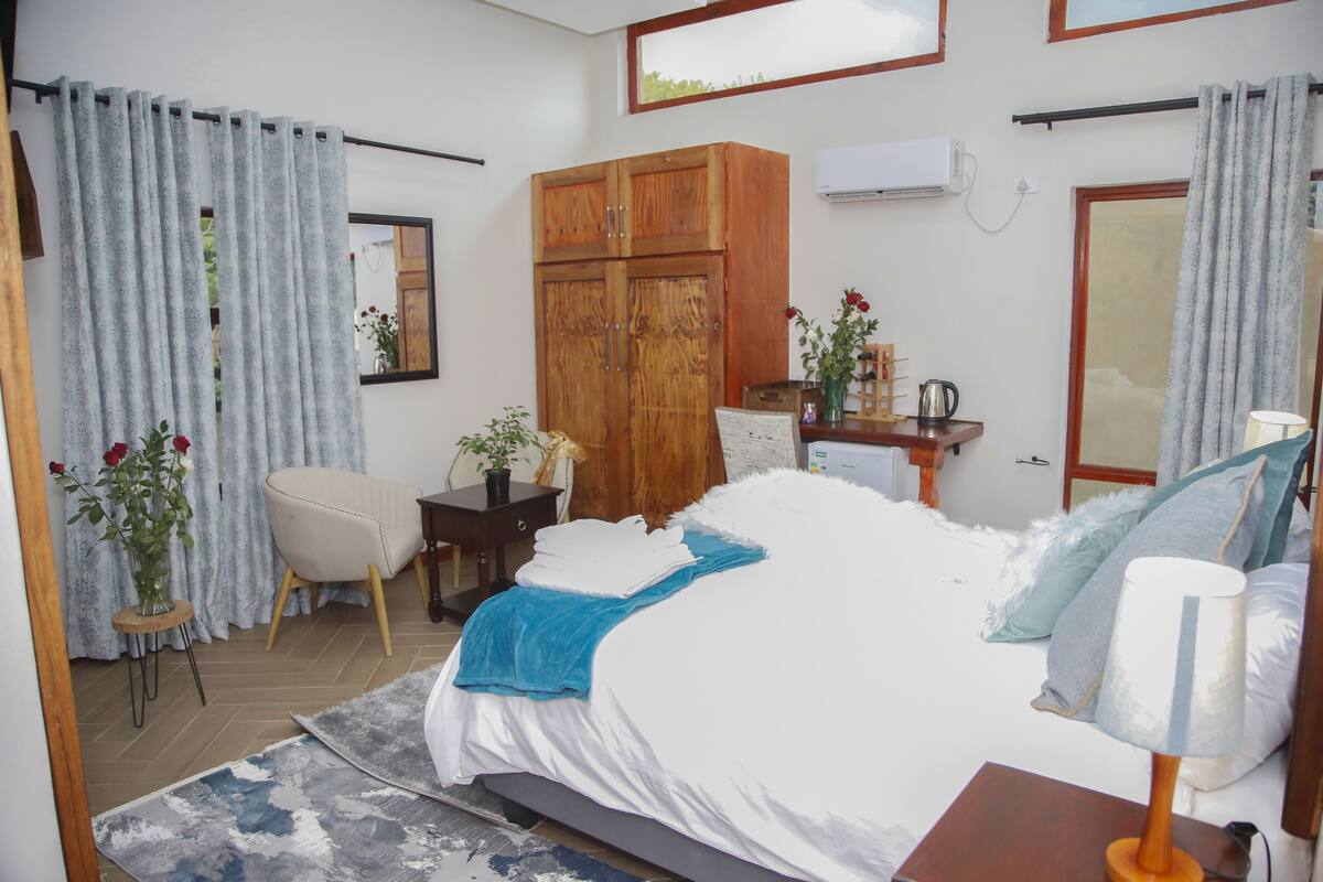 A bedroom with a bed, a wooden wardrobe, a desk with a lamp, and a chair.