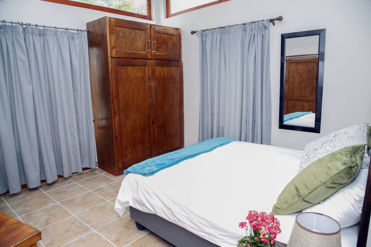 A bedroom with a bed, curtains, a wardrobe, and a mirror.