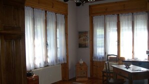 A room with wooden walls and floors, a dining table with chairs, a radiator, and a small cabinet. - Val di Cogne apartment (Vieyes)