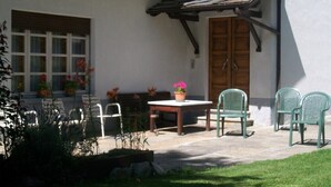 A patio with a table and chairs, a wooden door, and a window with curtains. - Val di Cogne apartment (Vieyes)
