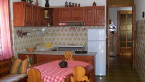 A kitchen with wooden cabinets, a stove, and a refrigerator. There is a dining table with chairs and a red tablecloth. - Val di Cogne apartment (Vieyes)