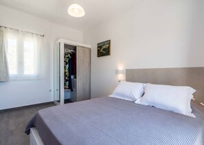 A bedroom with a bed, a wardrobe, a window with curtains, and a painting on the wall. - Aegiis maisonnettes - Baritis (Milos)