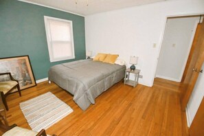 Ein Schlafzimmer mit Bett, Nachttischen, einem Sessel, einem Fenster und einer Tür.