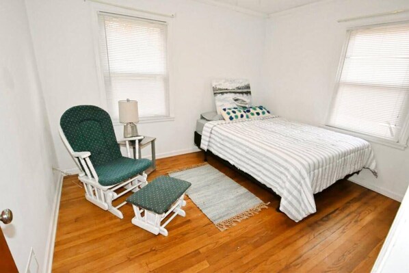 Un dormitorio con una cama individual, una silla, una mesita y una ventana.