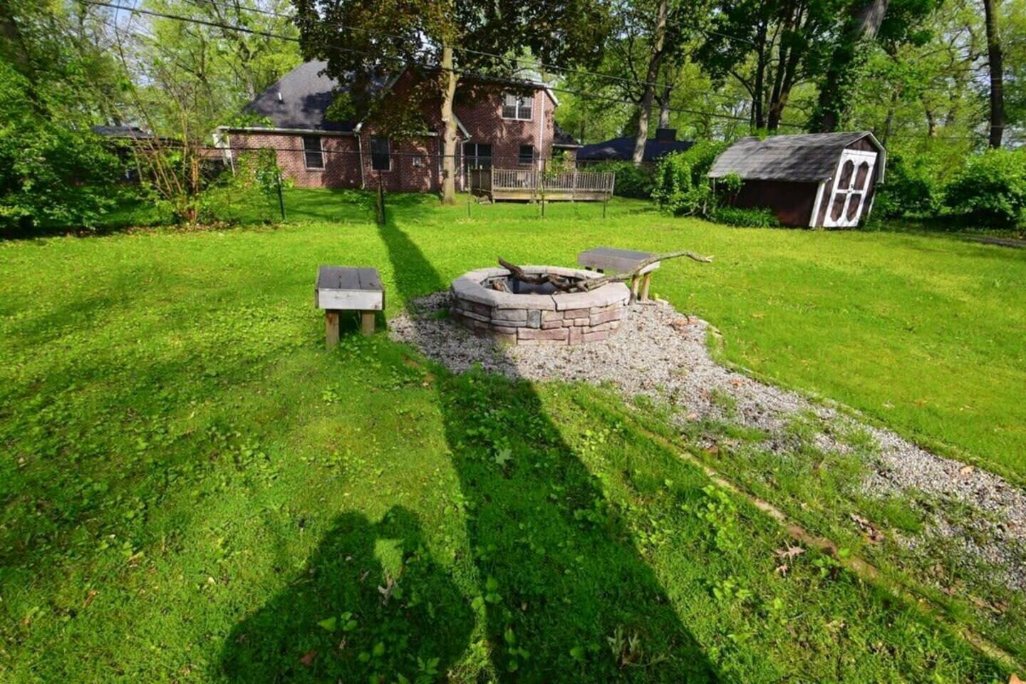 Un jardin avec un foyer en pierre, un banc en bois et un petit abri de jardin.