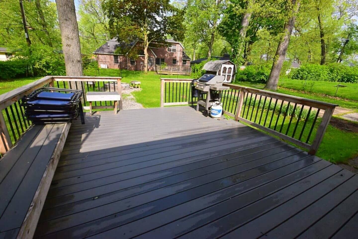 Une terrasse en bois avec un barbecue, un banc et un petit abri de jardin.