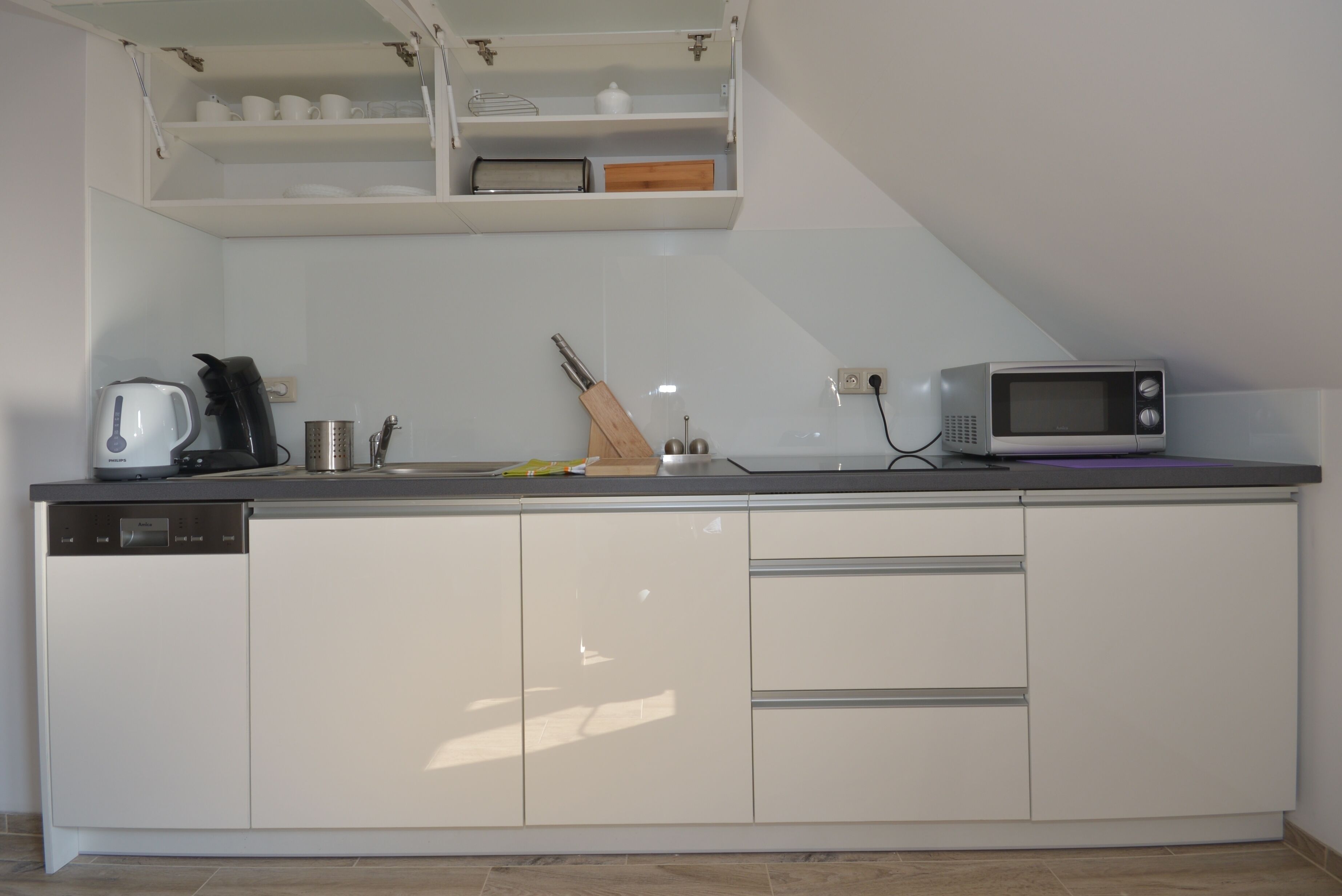 A modern kitchen with white cabinetry, a built-in microwave, and a kettle.