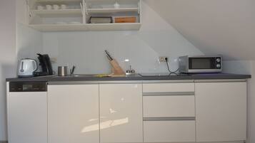 A modern kitchen with white cabinetry, a built-in microwave, and a kettle.