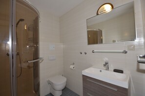 A modern bathroom with a glass shower enclosure, a toilet, a sink with a mirror above it, and a towel rack.