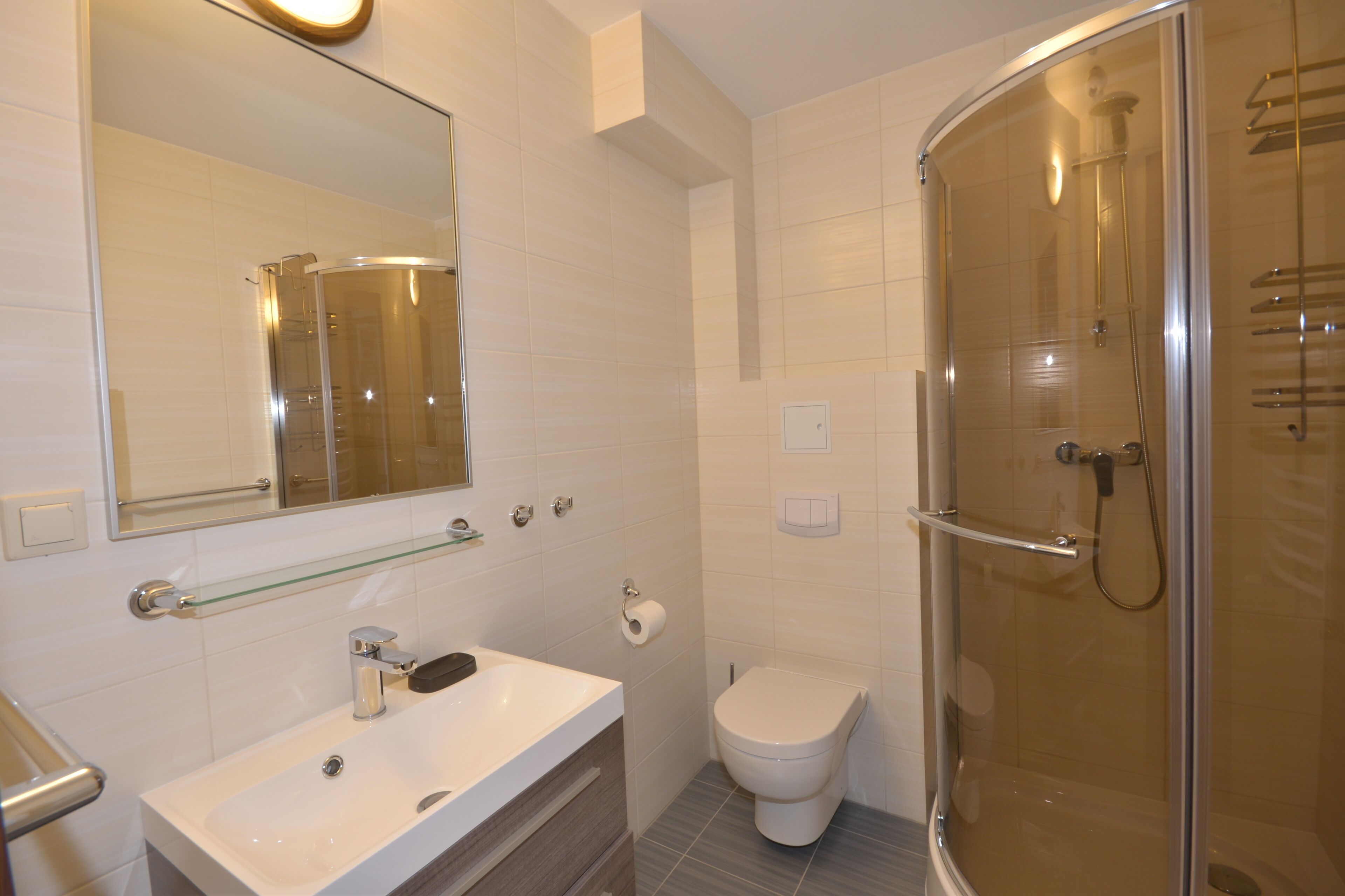 Un baño moderno con ducha de vidrio, lavamanos blanco y retrete.