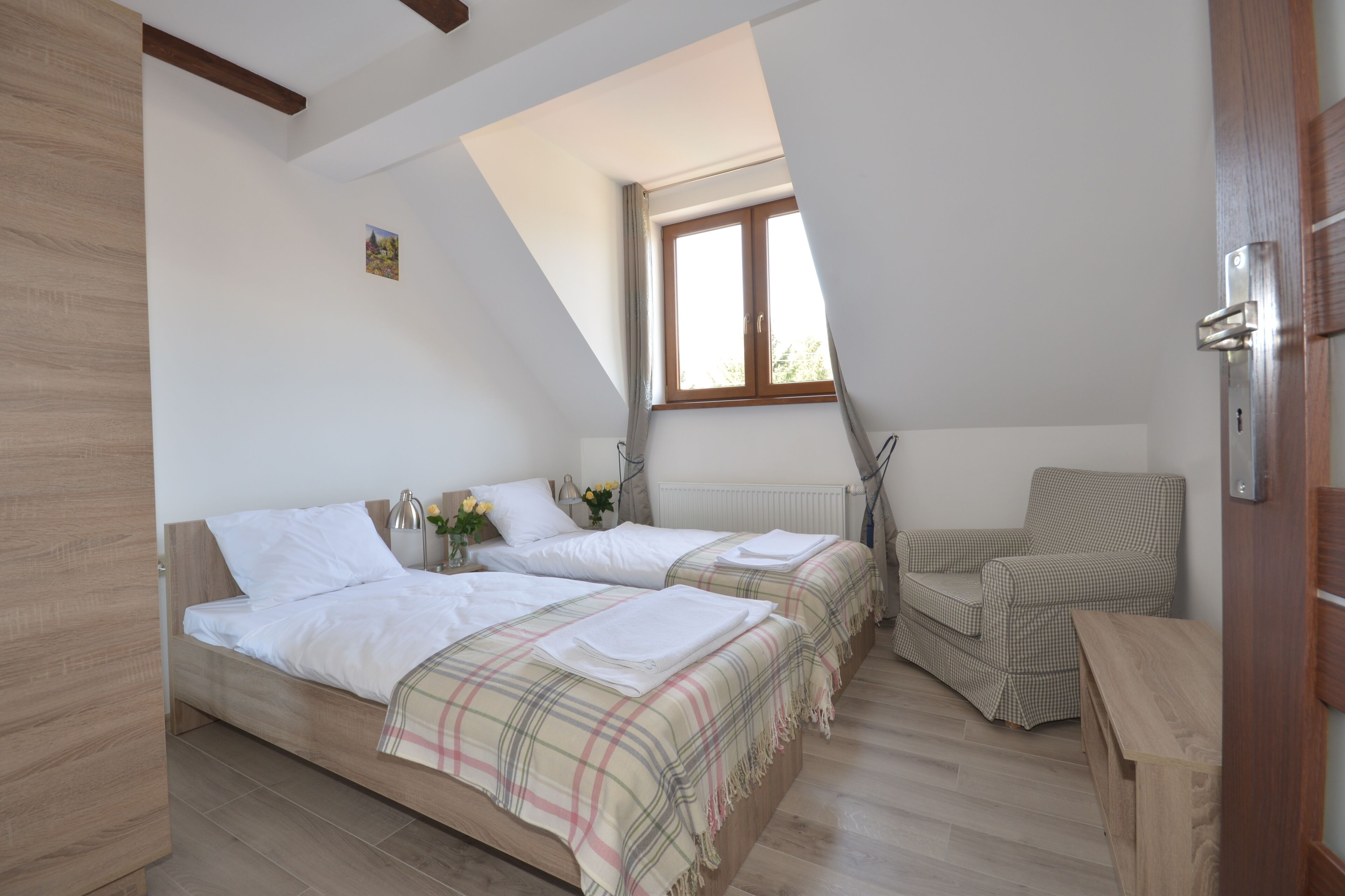 A bedroom with two beds, a window, a radiator, and a chair.