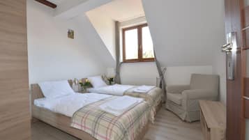 A bedroom with two beds, a window, a radiator, and a chair.
