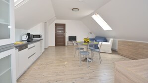 Una cocina moderna con armarios blancos, un comedor con mesa y sillas, y una sala de estar con sofá y televisor.