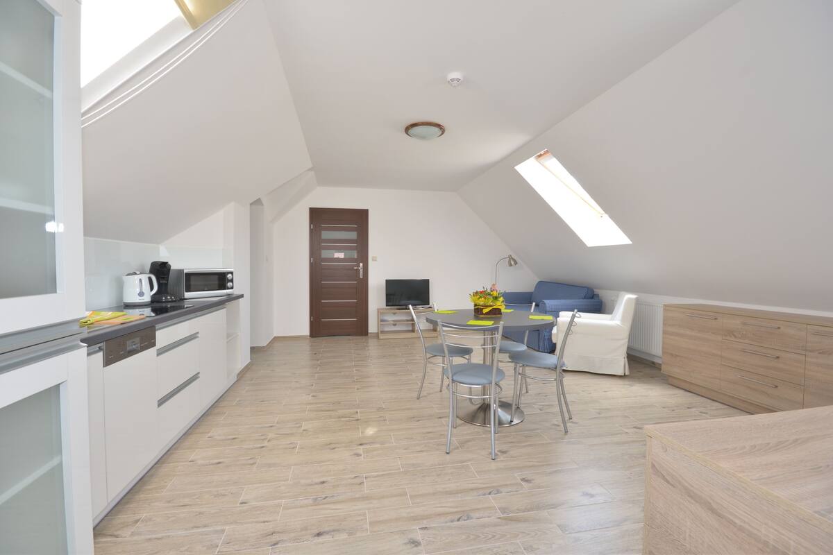 A modern kitchen with white cabinets, a dining area with a table and chairs, and a living space with a sofa and a TV.