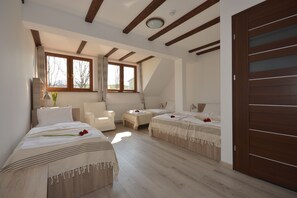 A bedroom with two beds, a chair, a small table, and a large window.