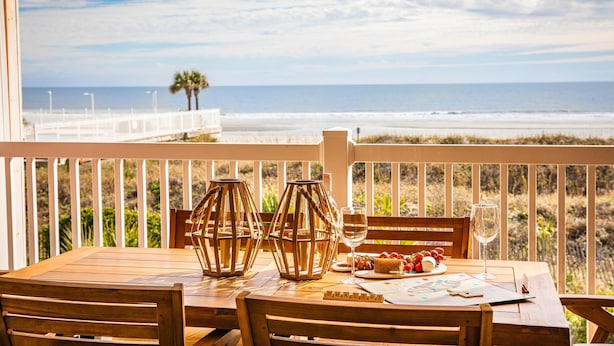 A wooden table with chairs on a balcony overlooking a beach. - Oceanfront Condo w/ Dual Balconies + Walk to Folly Pier (Folly Beach)