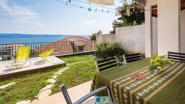 A terrace with a table set for dining, a yellow chair, and a view of the sea.