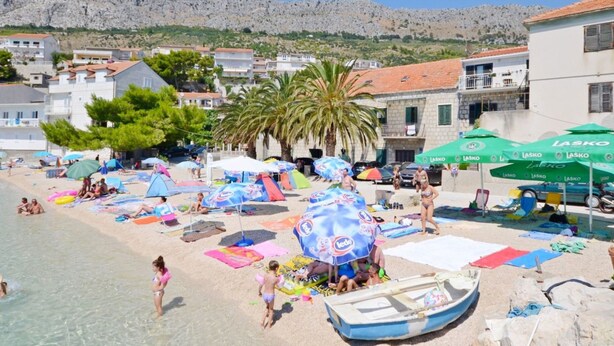 Una playa con sombrillas, gente y un bote.