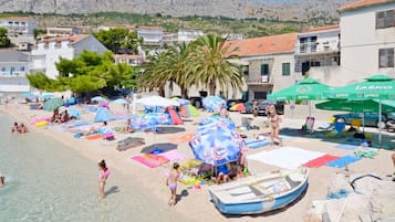 Una playa con sombrillas, gente y un bote.