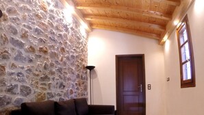 Una habitación acogedora con pared de piedra, techo de madera, un sofá marrón oscuro, una mesita y una puerta.