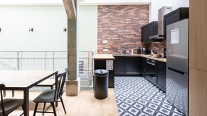 A compact kitchen with a brick backsplash, modern appliances, and a dining area with a view to the outside. - PHILIPPE AUGUSTE LOFT 1 - Loft for 12 - 5 rooms - BASTILLE - PÈRE LACHAISE (Paris)