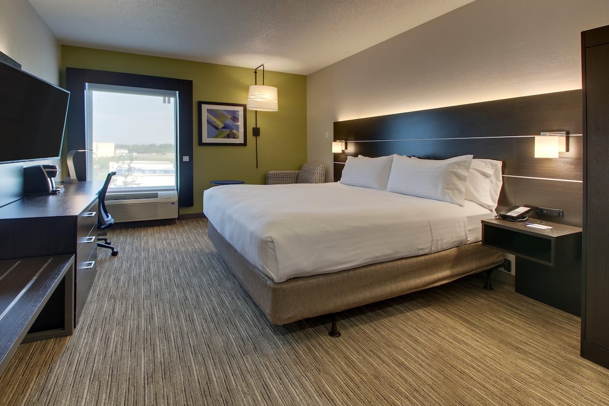A hotel room with a bed, desk, chair, and a large window.