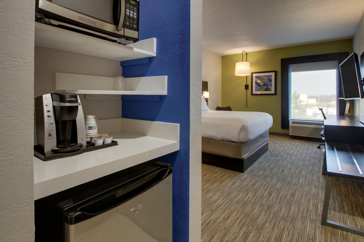 Quarto de hotel com cozinha compacta, cama, escrivaninha e janela com vista.