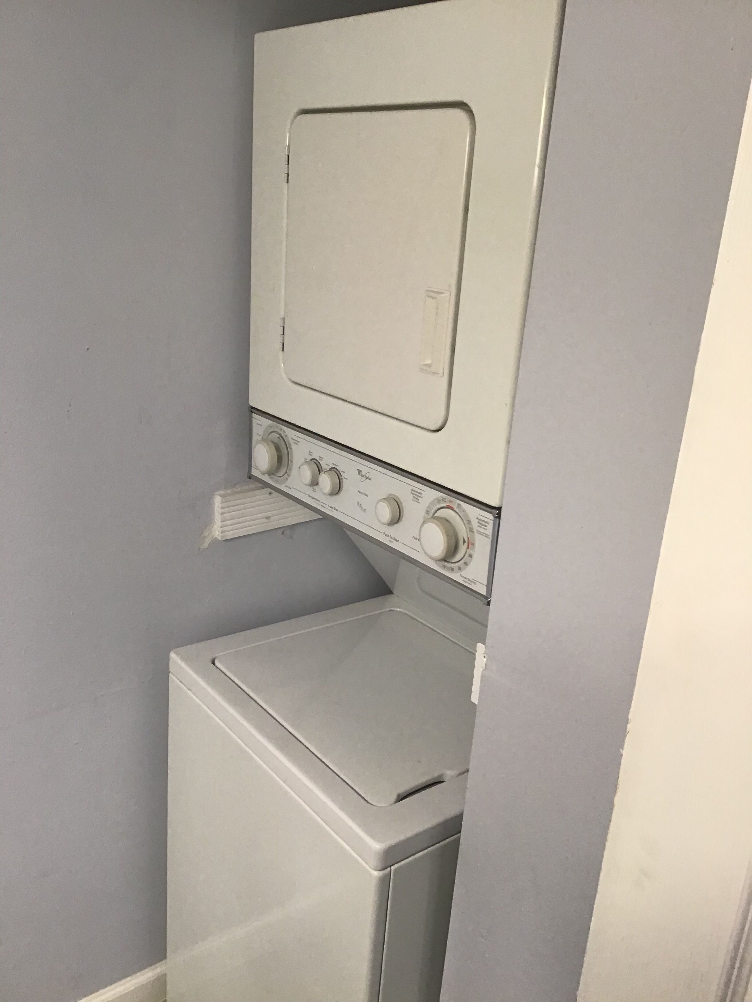 Une petite buanderie blanche, équipée d’un lave-linge et d’un sèche-linge superposés.