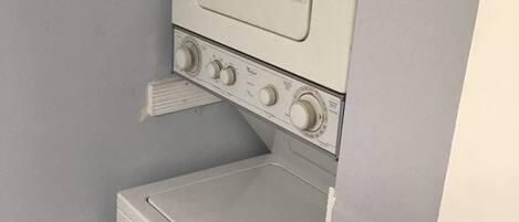 Une petite buanderie blanche, équipée d’un lave-linge et d’un sèche-linge superposés.