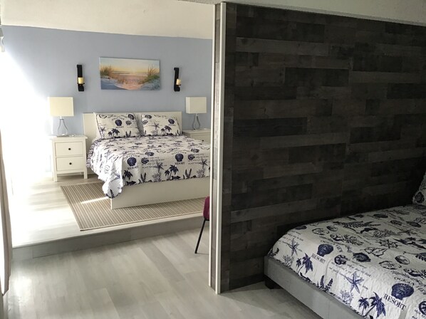 A bedroom with a bed, a nightstand, a lamp, a wall-mounted clock, and a painting.