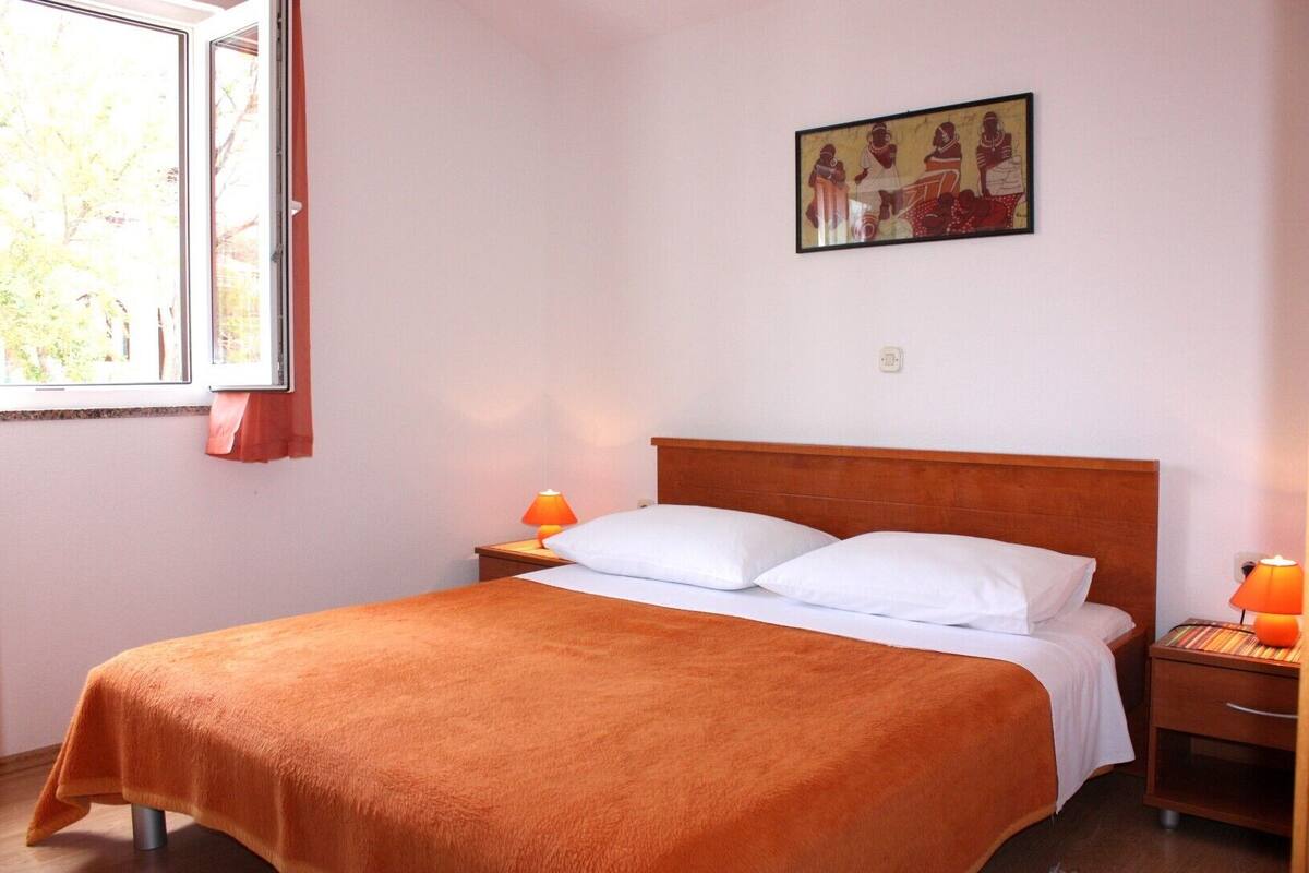 A hotel room with a single bed, two bedside tables, a window, and a wall-mounted painting.