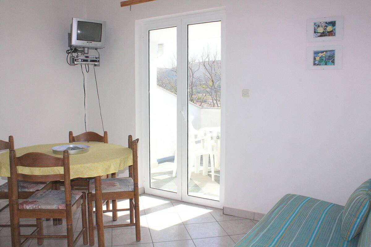 A dining area with a table and chairs, a television mounted on the wall, and a sliding glass door leading to an outdoor patio.