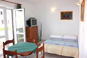 A room with a bed, a table with chairs, a television on a cabinet, and a colorful painting on the wall. - Apartment VIZ (Pag)