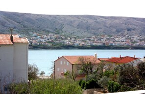 Uma cidade costeira com edifícios ao longo da água, uma colina ao fundo e vegetação em primeiro plano.