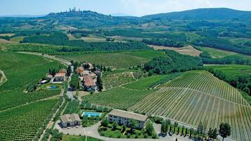 Une vue aérienne d’un vignoble avec des terrasses et un ensemble de bâtiments, dont une grande maison en pierre et des constructions plus petites, le tout entouré d’une végétation luxuriante et de collines ondulantes.