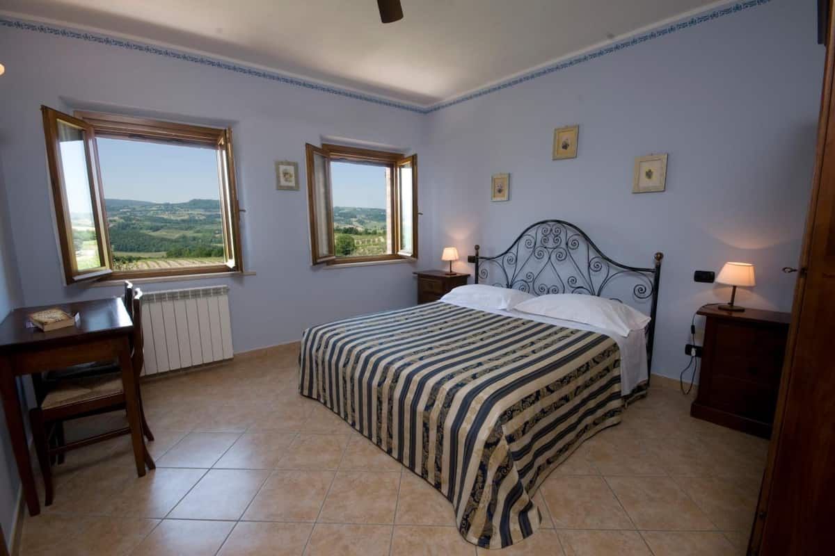 A bedroom with two windows, a bed with a striped bedspread, a desk, and a chair.