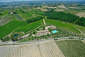 An aerial view of a vineyard with terraced fields, a large building with a swimming pool, and a road running through the property. - Agriturismo Macinatico 1 (San Gimignano)