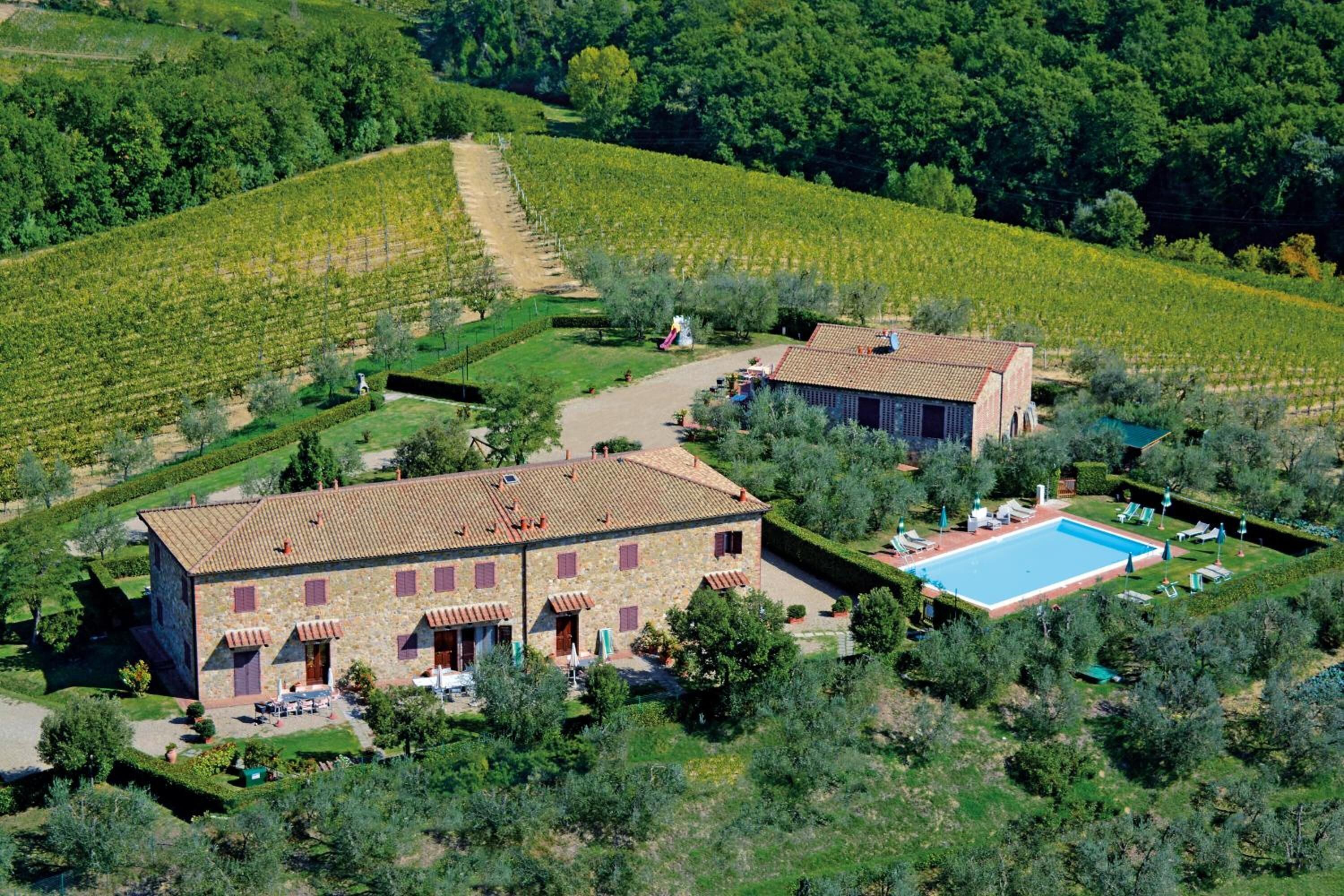 A stone building with a tiled roof, a swimming pool, and a vineyard in the background.