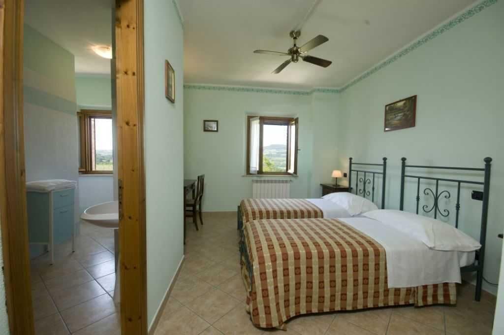 A bedroom with two beds, a ceiling fan, a window, and a radiator.