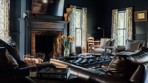 Un salon à l’ambiance sombre, doté d’une cheminée, de meubles en cuir et de livres.