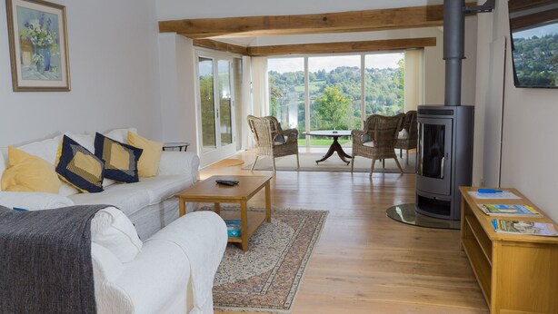 A spacious living room with a white sofa, two wicker chairs, a wooden coffee table, and a large black wood-burning stove. - The Retreat (Stroud)