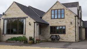 A stone house with a large window and a smaller window, two doors, and a patio with chairs. - The Retreat (Stroud)