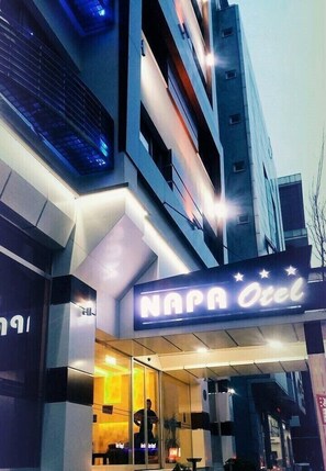 A hotel entrance with a neon sign, glass doors, and a modern building facade. - Napa Otel (Denizli)