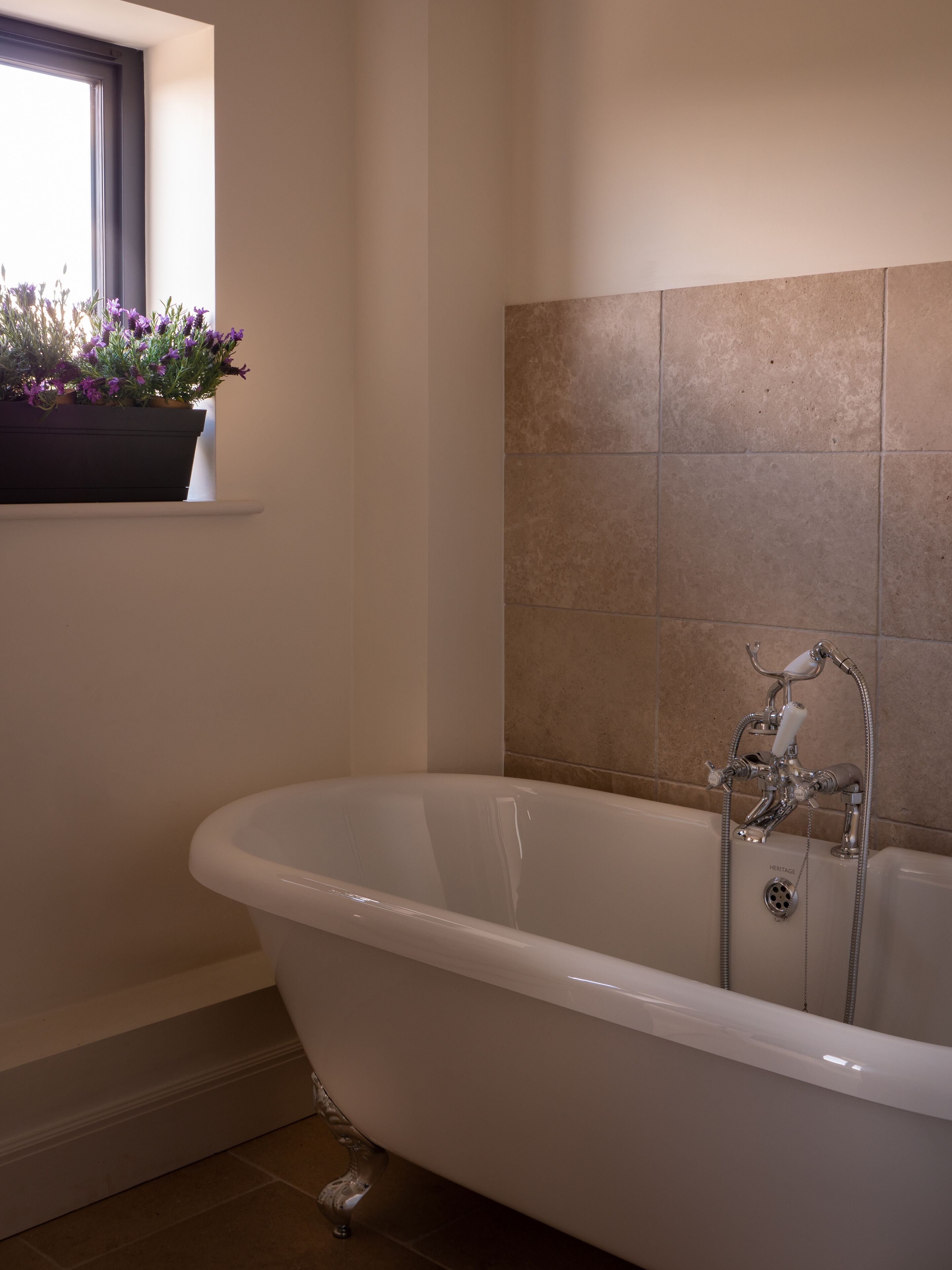 A modern bathroom with a freestanding bathtub, a window with a flower box, and tiled walls.