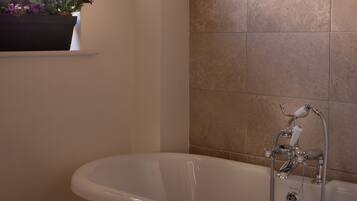 A modern bathroom with a freestanding bathtub, a window with a flower box, and tiled walls.